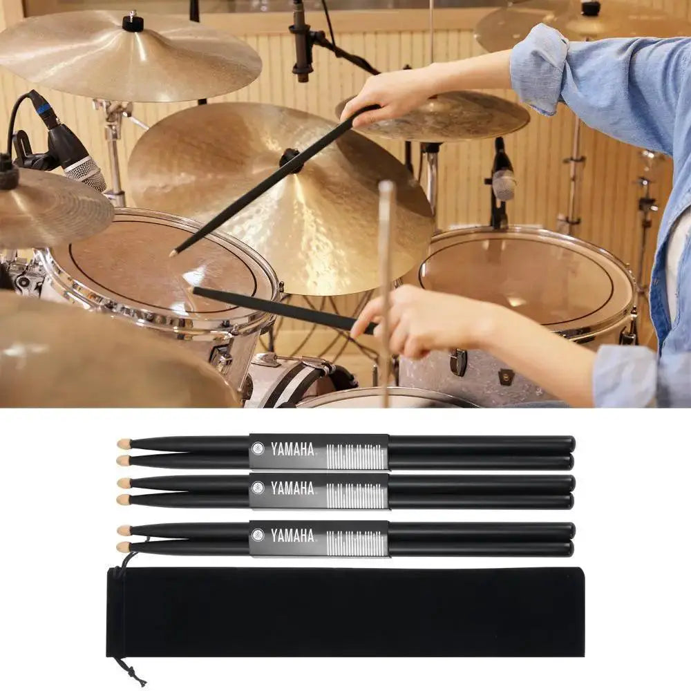 Black wooden drum sticks set with carrying bag, shown with acoustic drum kit.