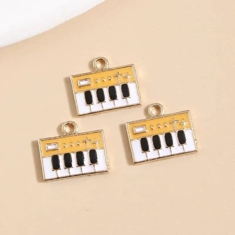 Three enamel keyboard charms with gold trim for DIY jewelry on a beige background, OurLum.com