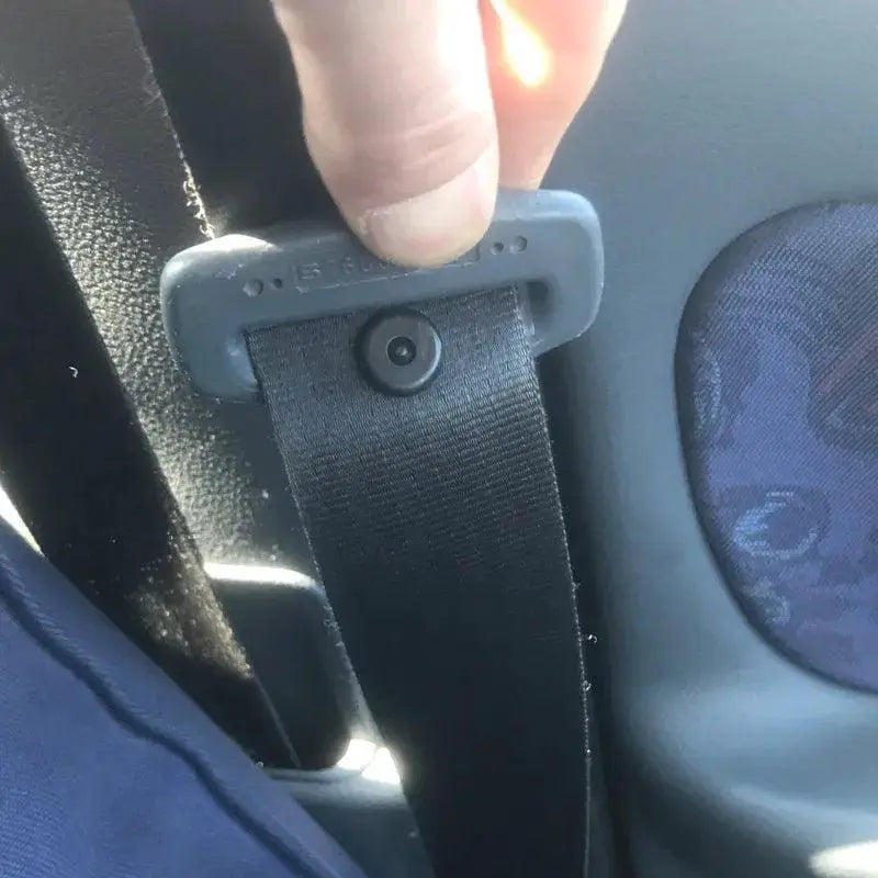 Close-up of a hand holding a black car seat belt with a plastic stopper inside a vehicle