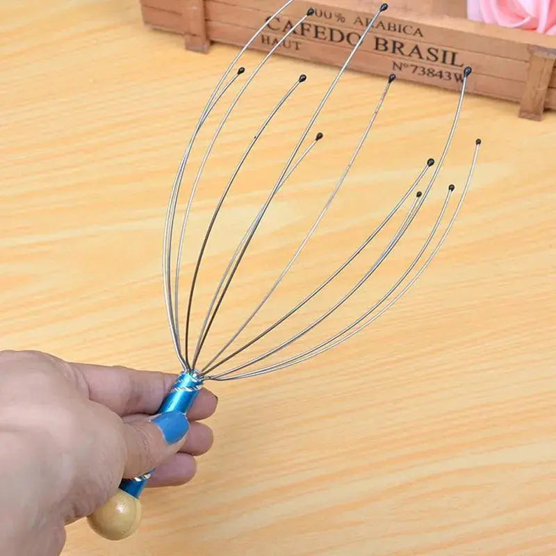 Hand holding a metal octopus scalp massager with wooden handle on a light wood table.
