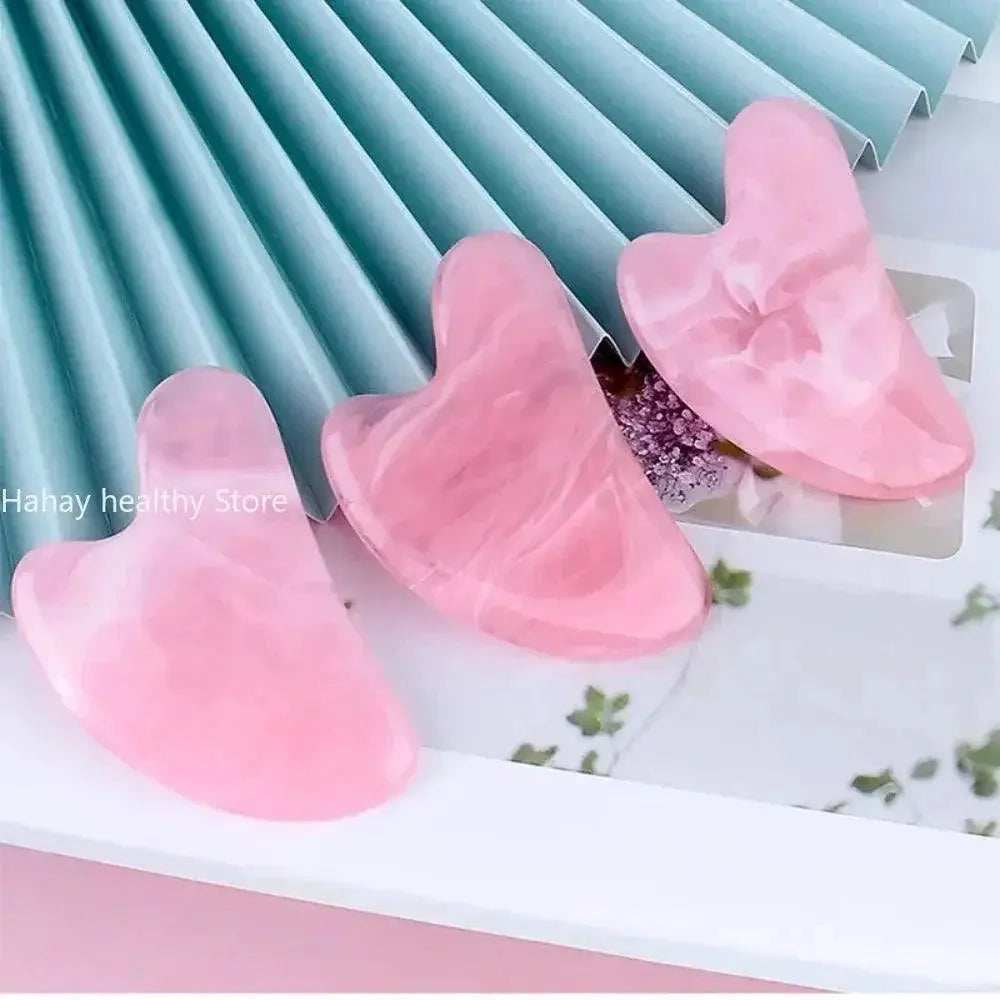Three pink crystal gua sha facial massage tools on a decorative background