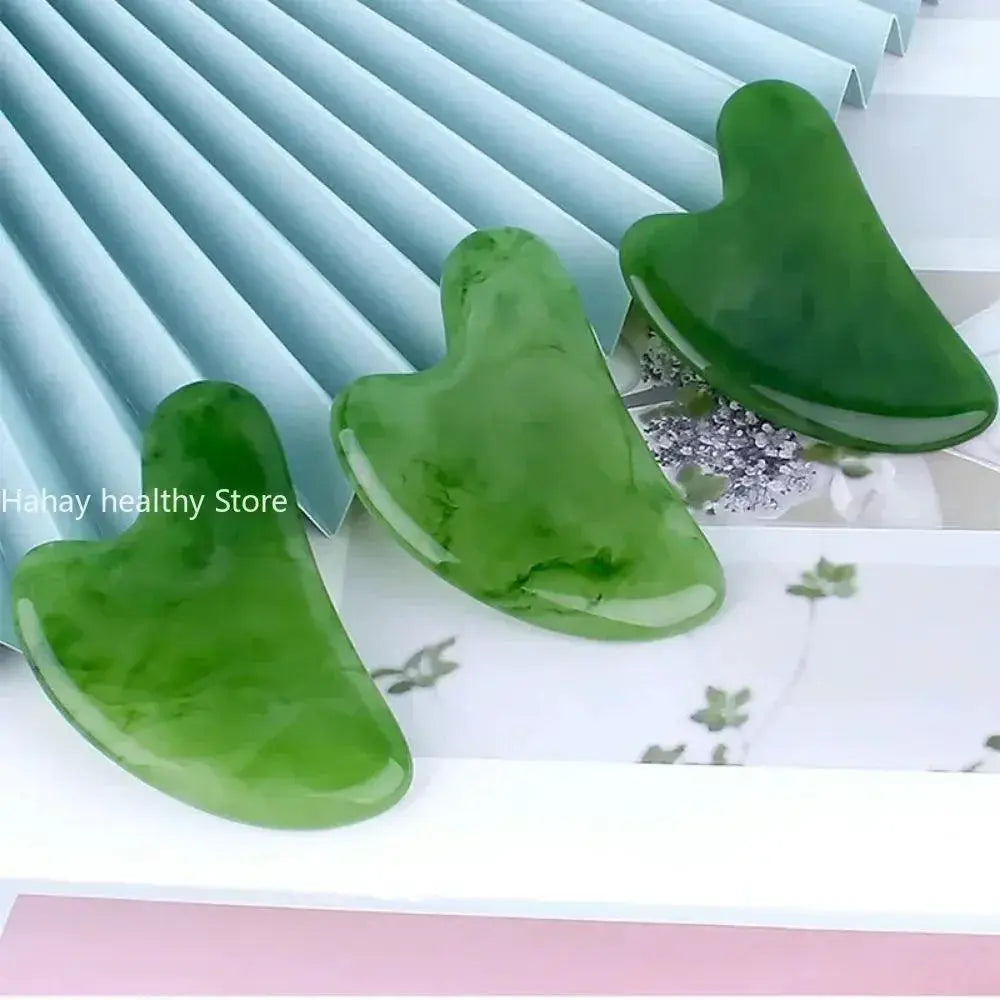 Three green jade gua sha facial massage tools on a pastel background for skincare