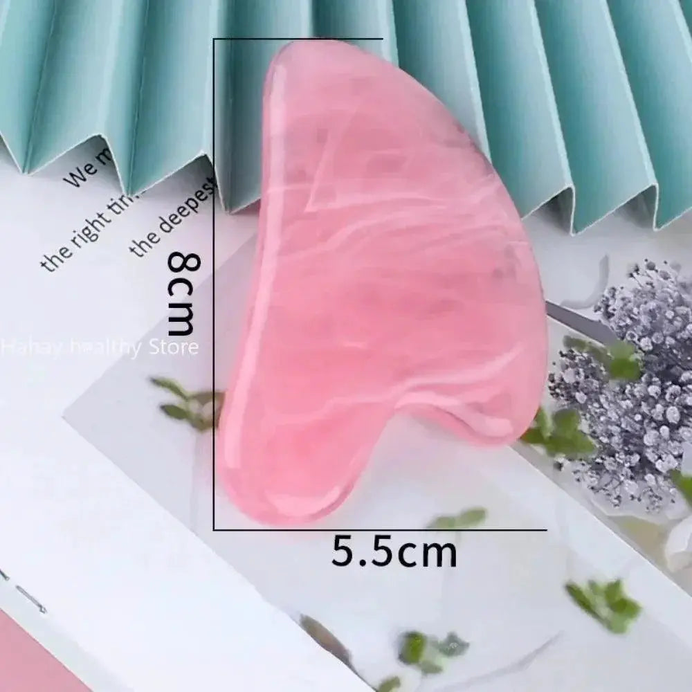 Pink crystal gua sha stone for facial massage, measuring 8cm by 5.5cm, on a paper surface