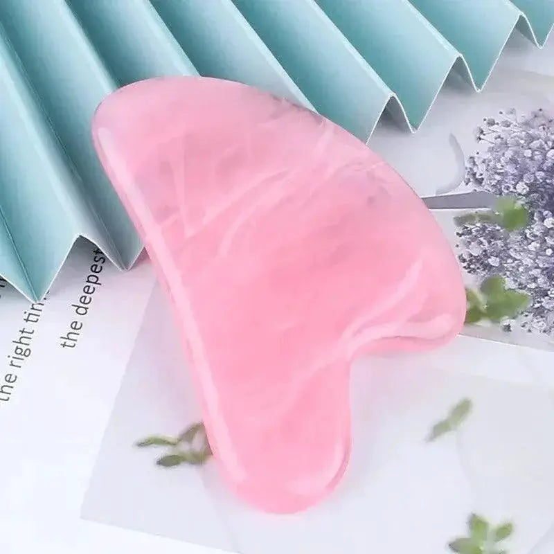 Pink rose quartz gua sha stone facial massage tool on a light background